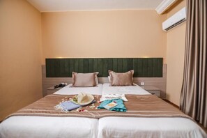 Una habitación de hotel con cama, mesitas de noche, aire acondicionado y una cortina.