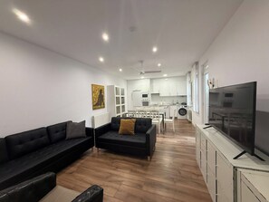 A modern living room with a black sofa, a small black ottoman, and a television on a white cabinet. - Spacious flat in  centre of the Barrio del Oeste (Salamanca)