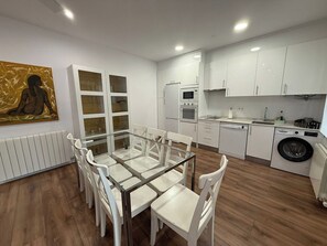 Eine moderne Küche mit weißen Schränken, einem Esstisch mit Stühlen, einem Bild an der Wand und einer Heizung.