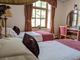Habitación de hotel con dos camas, un escritorio, una silla, una lámpara y una ventana con cortinas.