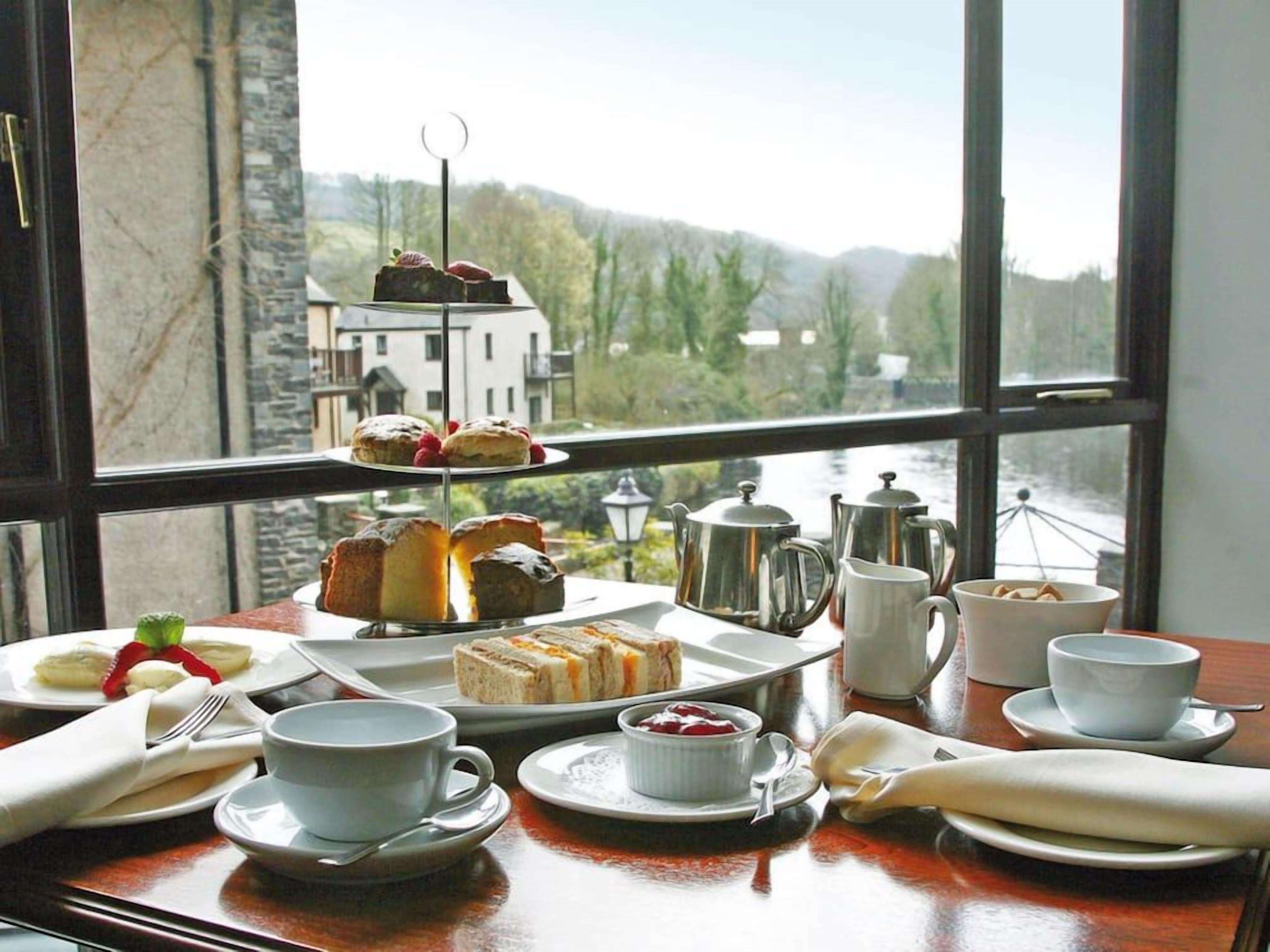 A table set with tea service and pastries, overlooking a scenic view through a large window.