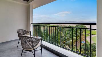 A balcony with two chairs and a table, overlooking a landscaped area with palm trees and a view of distant hills.