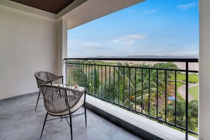 A balcony with two chairs and a table, overlooking a landscaped area with palm trees and a view of distant hills. - Lemon Tree Resort, Nashik (Nashik)