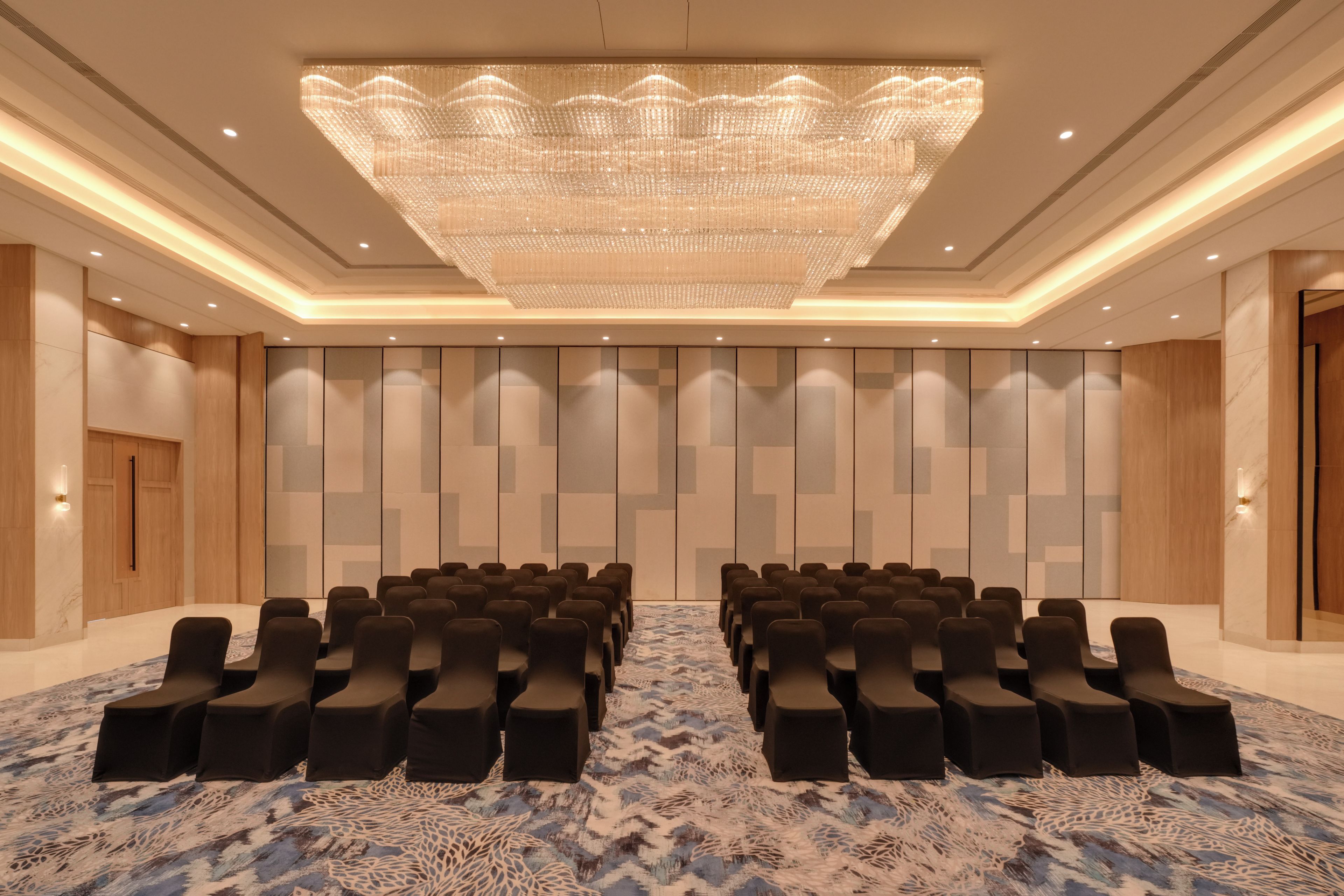 A conference room with rows of chairs, a large chandelier, and a patterned carpet.