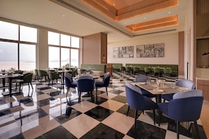 A spacious restaurant with a checkered floor, green booths, and a view of the sea. - Lemon Tree Resort, Nashik (Nashik)
