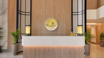 Un mostrador de recepción con un logotipo, dos lámparas de pared y plantas en macetas.