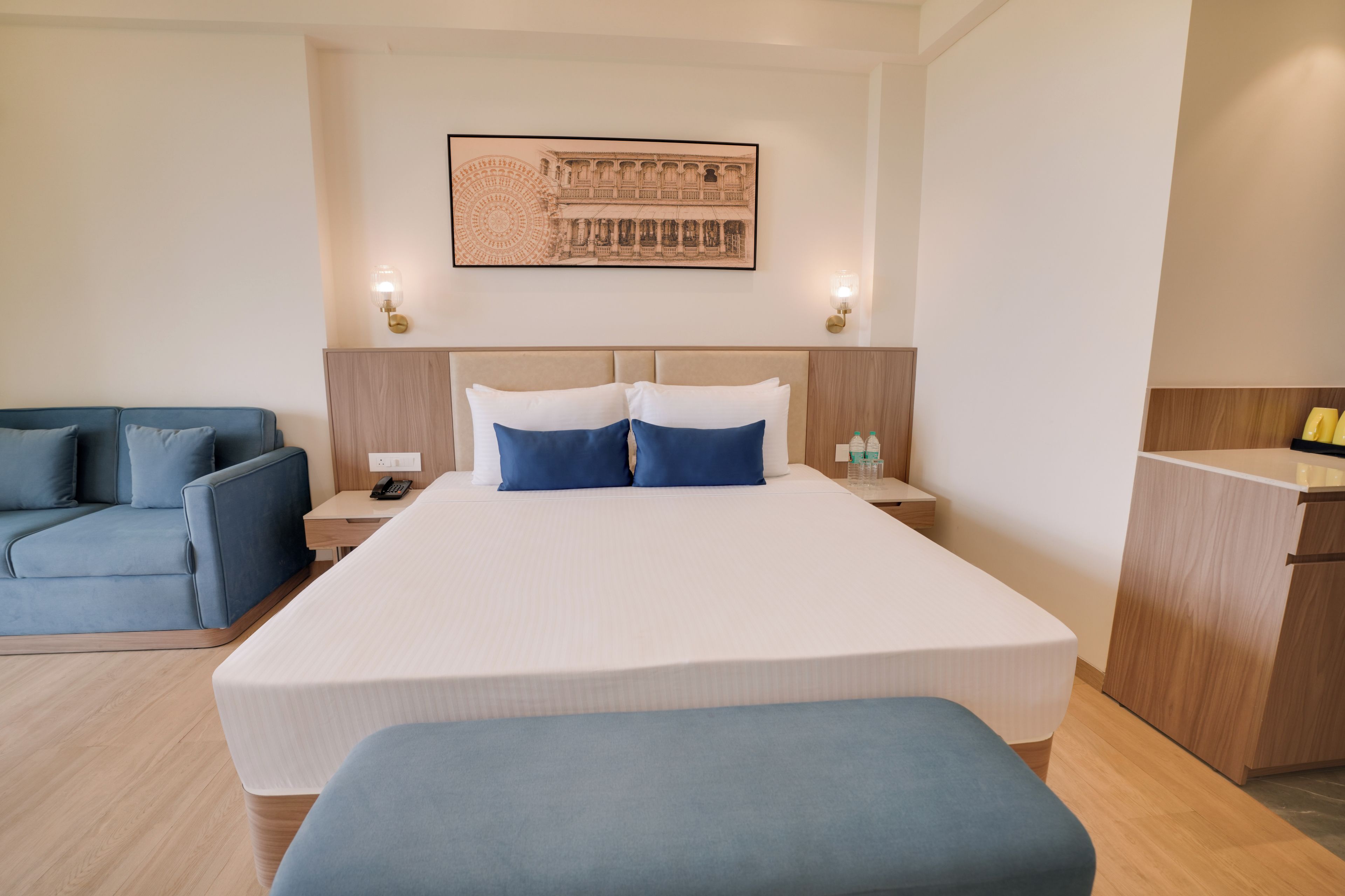 A hotel room with a large bed, a blue sofa, a desk, and a wall-mounted artwork.