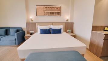 A hotel room with a large bed, a blue sofa, a desk, and a wall-mounted artwork.