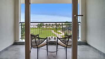 A balcony with two wicker chairs and a small table, overlooking a well-maintained lawn and a distant view of a body of water.