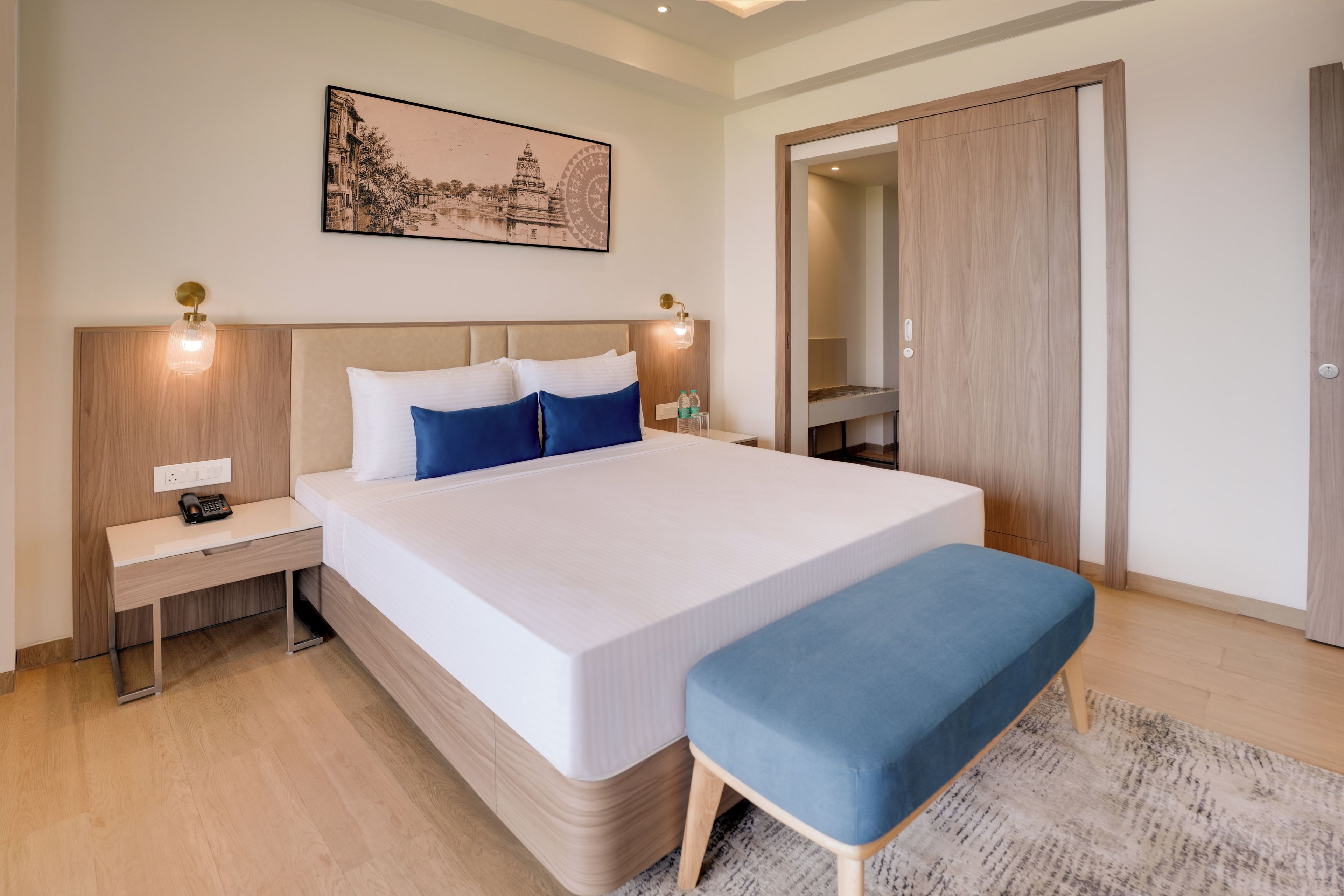Une chambre d’hôtel moderne avec un grand lit, des tables de chevet, une lampe de chevet, une petite table et un grand miroir.