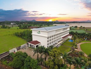 A resort with a large building, a swimming pool, and a view of the sunset over a body of water. - Lemon Tree Resort, Nashik (Nashik)