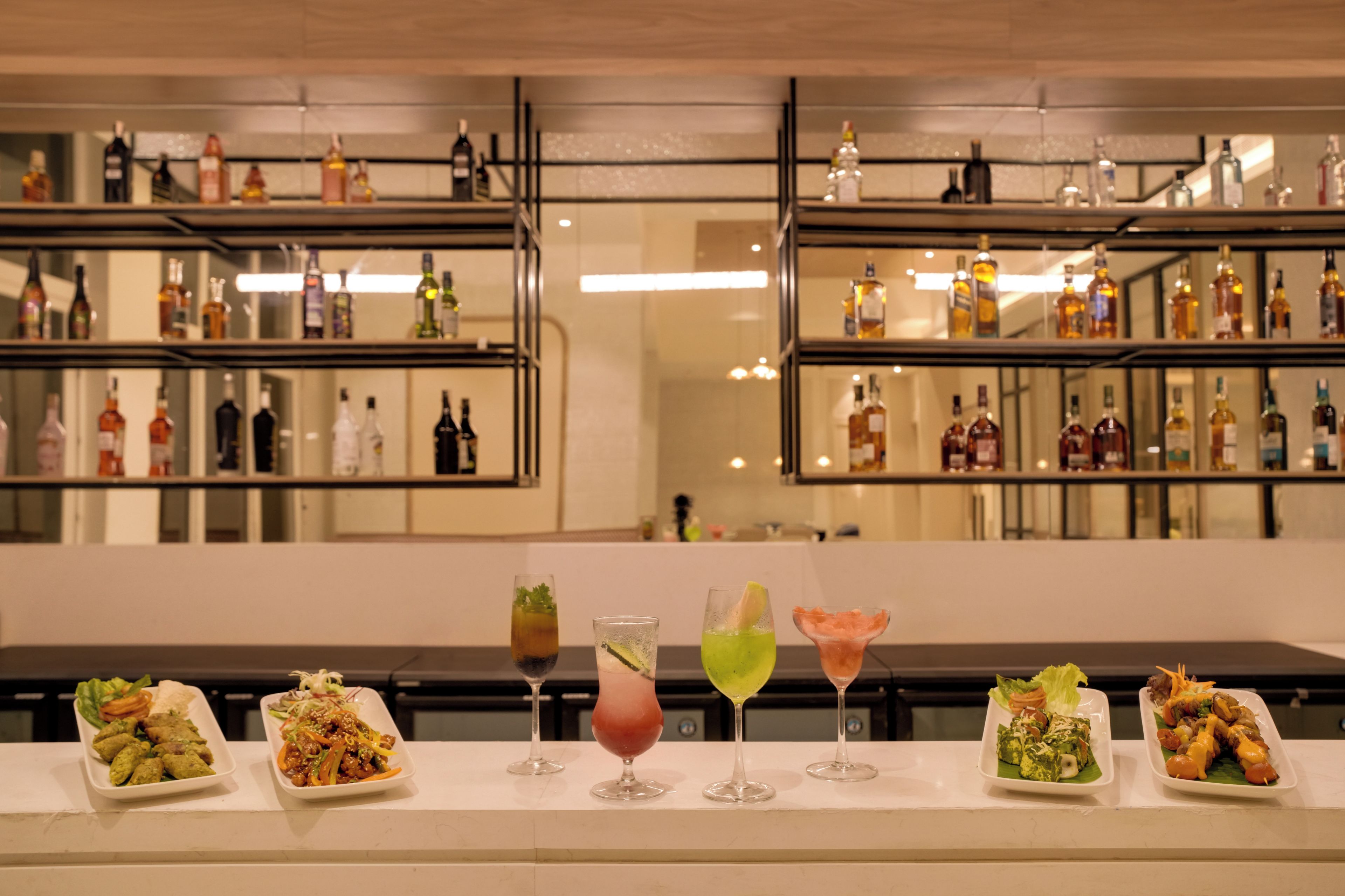 A bar area with multiple shelves of bottles and a variety of dishes and drinks on the counter.