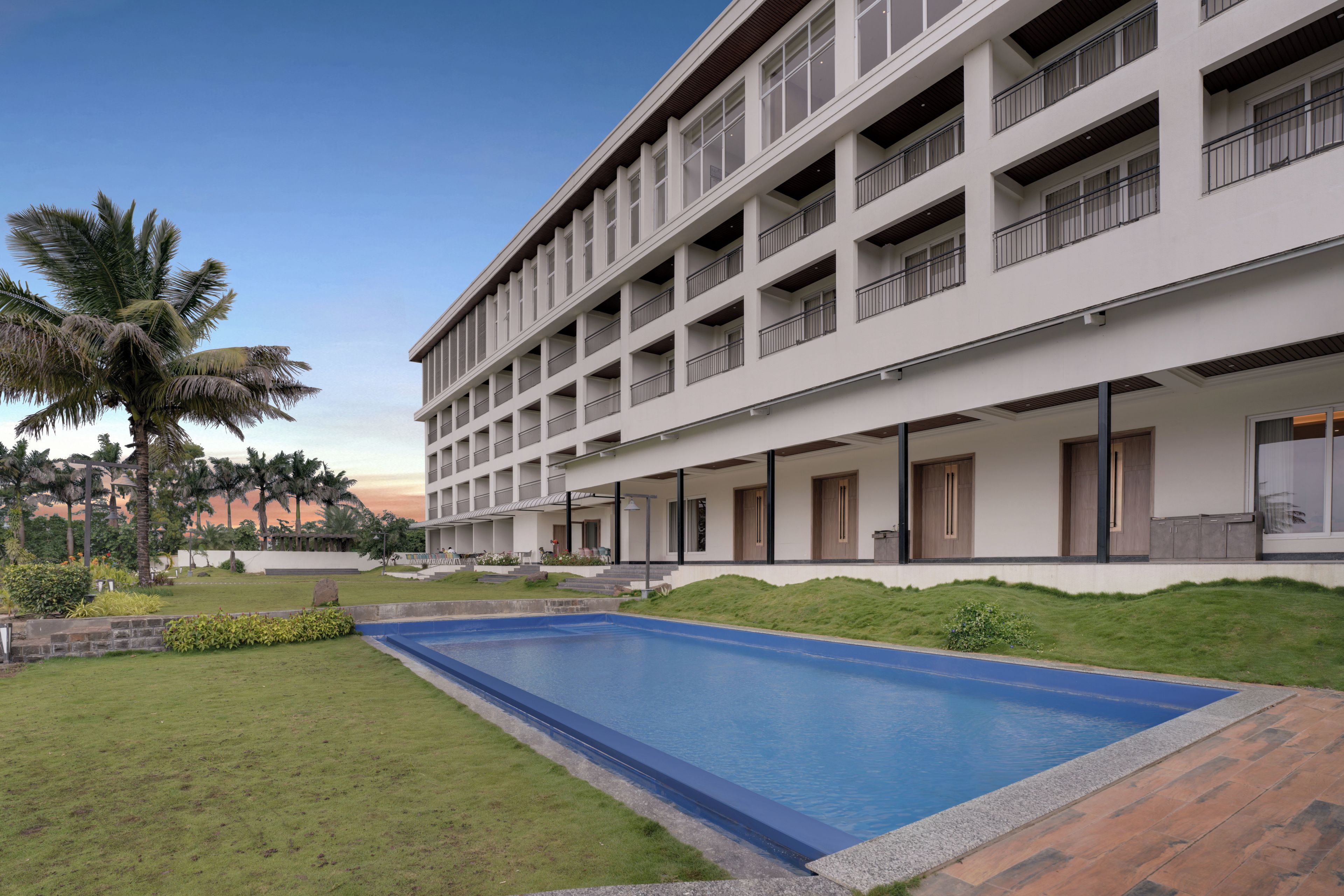 A multi-story hotel with a swimming pool, outdoor seating, and palm trees.