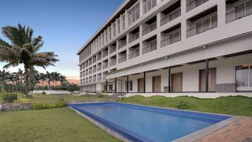 A multi-story hotel with a swimming pool, outdoor seating, and palm trees.