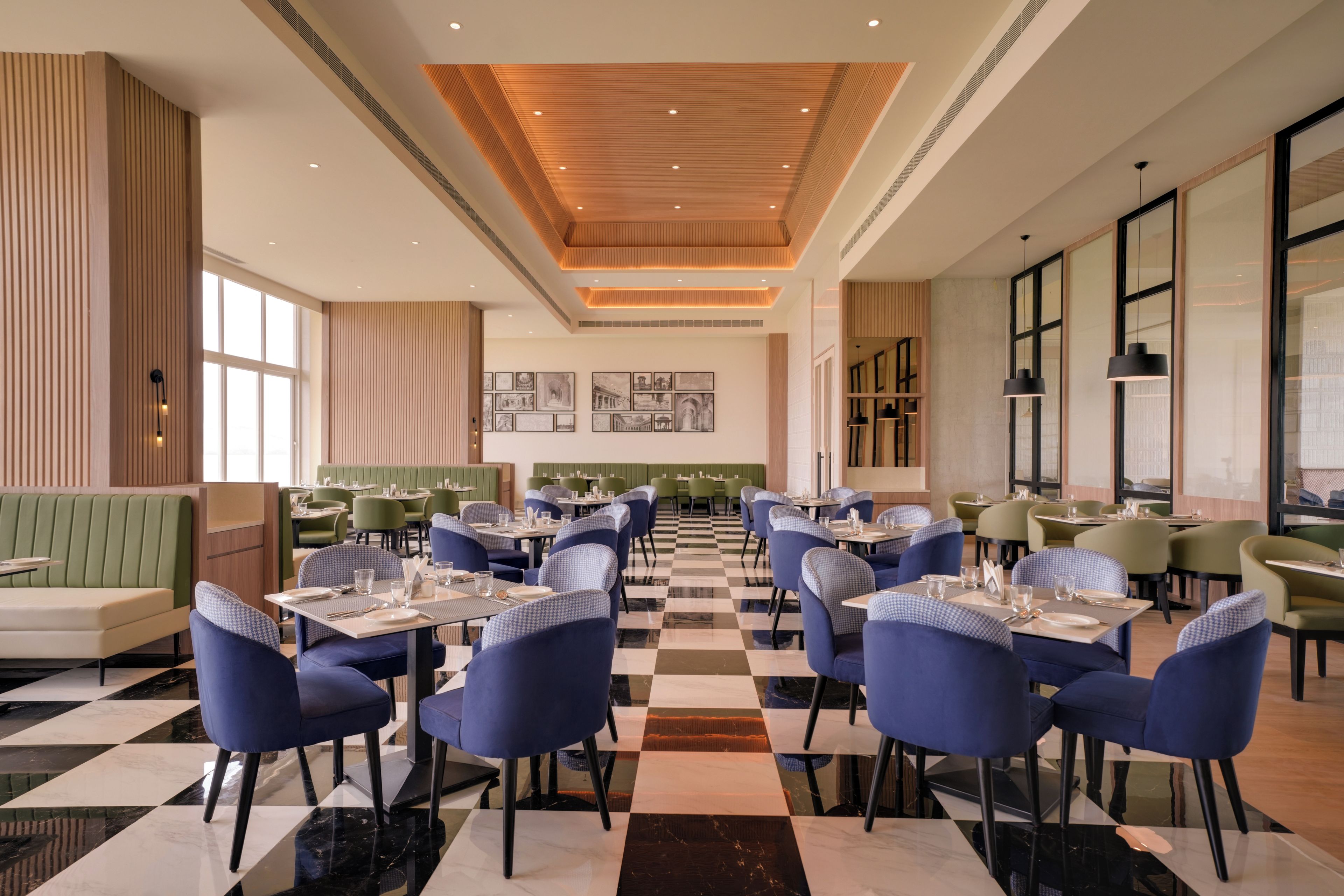 A restaurant with checkered flooring, blue upholstered chairs, and green booths.