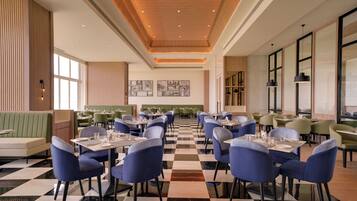 A restaurant with checkered flooring, blue upholstered chairs, and green booths.