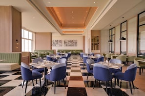 A restaurant with checkered flooring, blue upholstered chairs, and green booths. - Lemon Tree Resort, Nashik (Nashik)