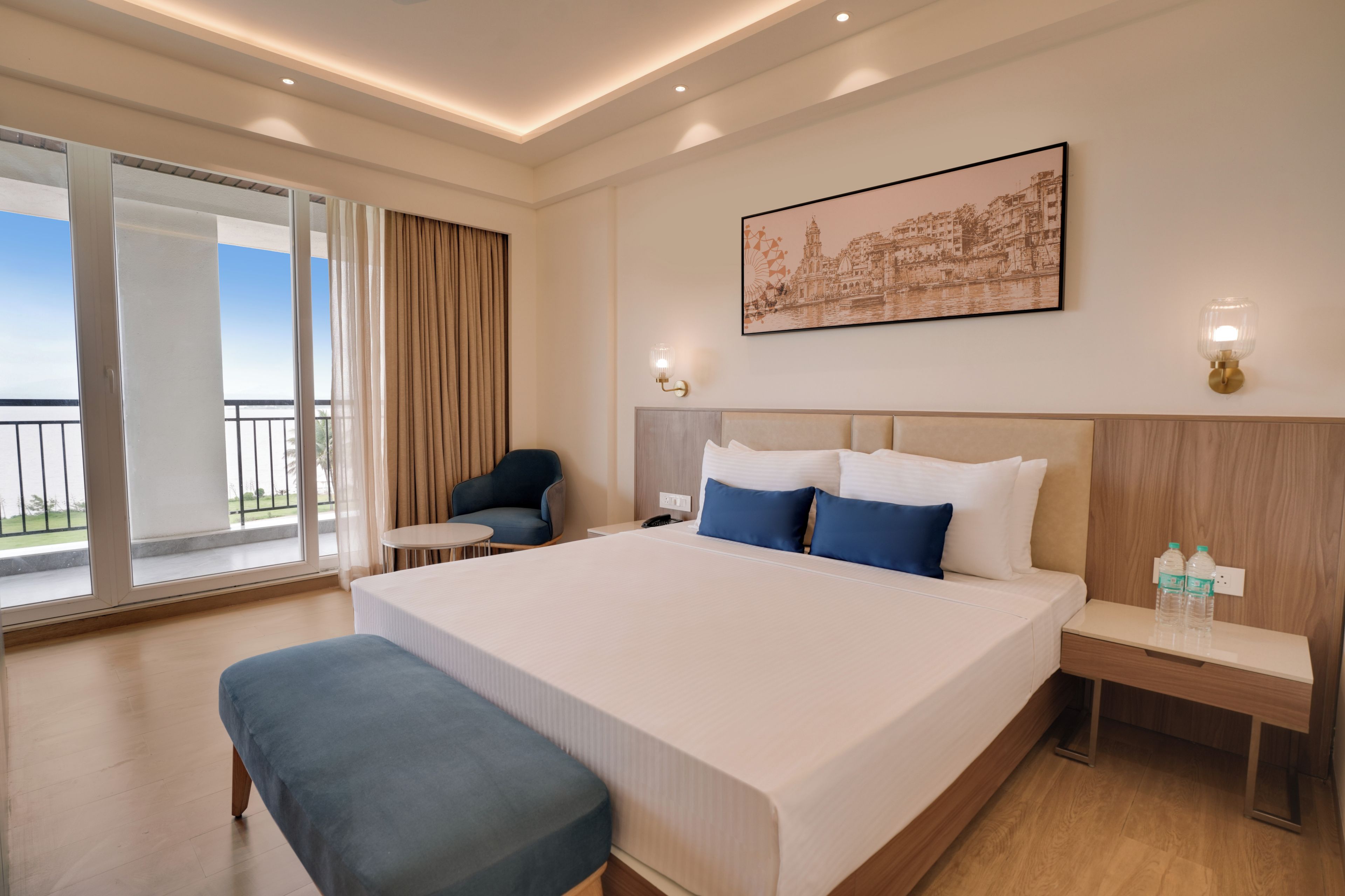A hotel room with a large bed, a chair, a table, a picture on the wall, and a view of the outdoors.