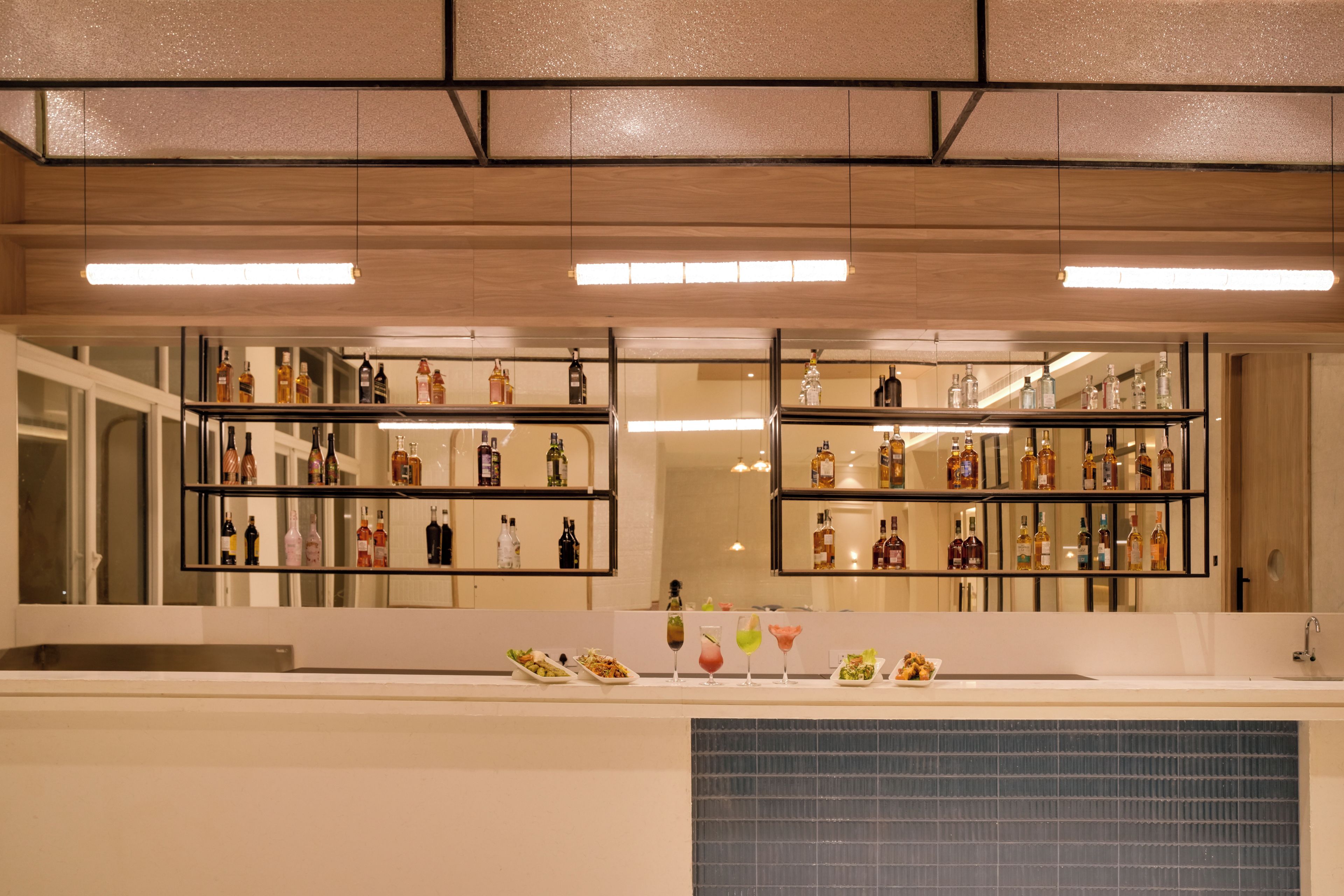 Zona de bar con estantes llenos de botellas de licores y una barra con comida y bebidas.