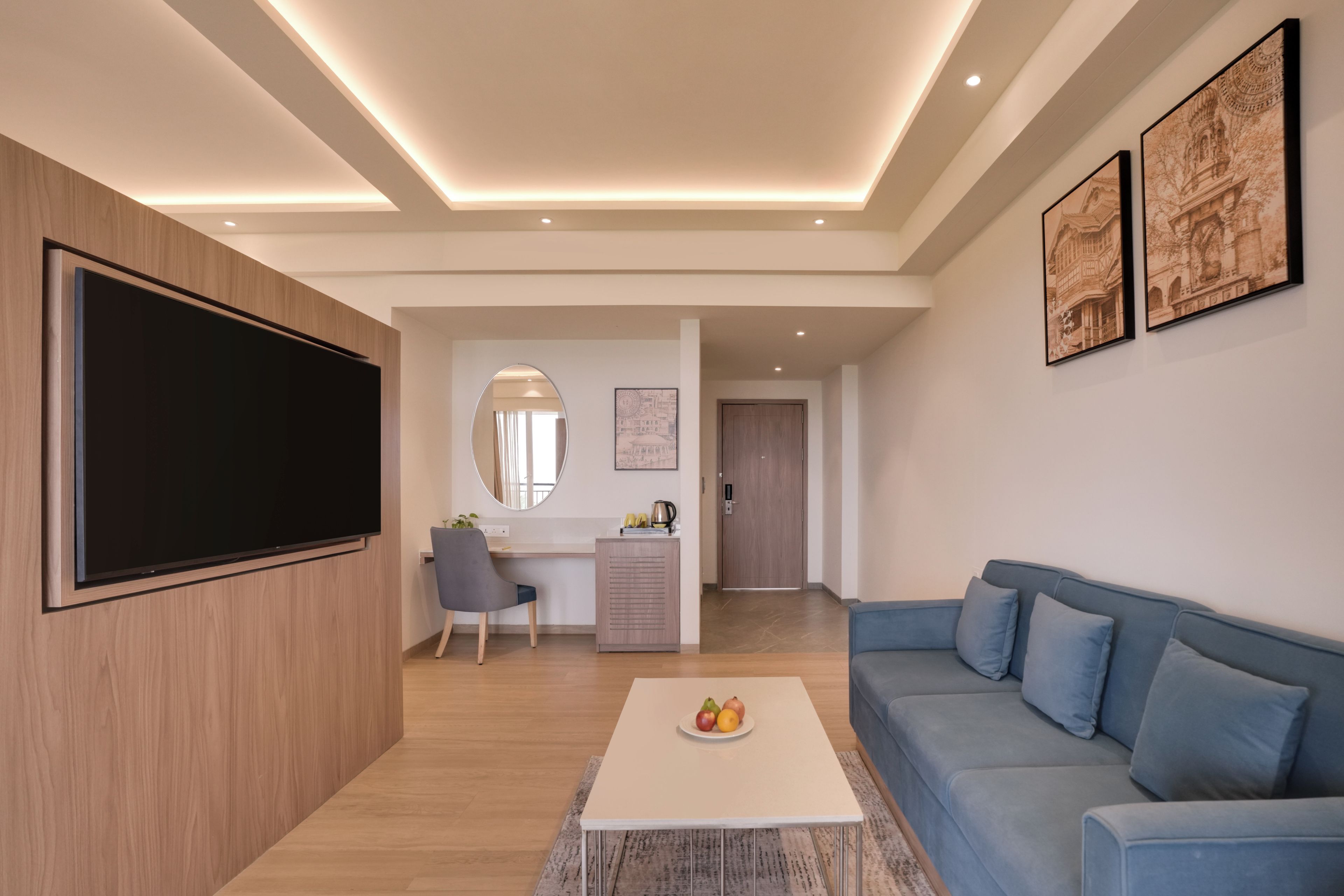 A modern living room with a flat-screen TV, a blue sofa, a coffee table with fruit, and artwork on the walls.