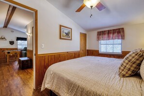 A bedroom with a large bed, wooden flooring, a ceiling fan, a window with blinds, and a door leading to another room. - Canopy View Lodge - Awesome Mountain Views, Hot Tub!!! (Sevierville)