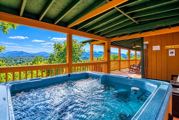 Un jacuzzi con vista a las montañas, una terraza de madera y un área de estar cubierta.
