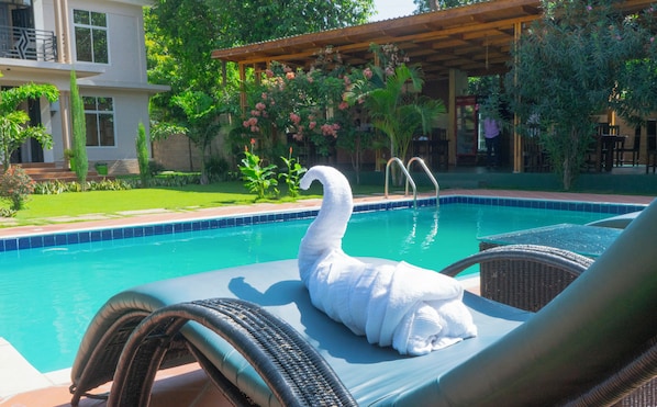 A pool with a swan-shaped towel, lounge chairs, and a garden area with trees and plants.