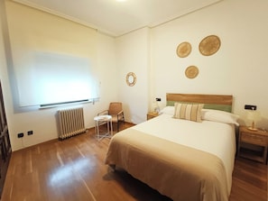 A hotel room with a bed, a chair, a small table, a radiator, and wall decorations. - Alojamiento Pl. del Ángel junto Pl. Mayor (Salamanca)