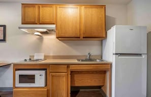 Een kleine keuken met houten kastjes, een magnetron, een spoelbak en een koelkast.