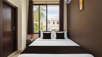 Habitación de hotel con cama, ventana con cortinas, un jarrón con flores y un cuadro en la pared.