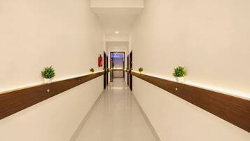 A long, narrow hallway with a wooden floor and white walls, leading to a door at the end.