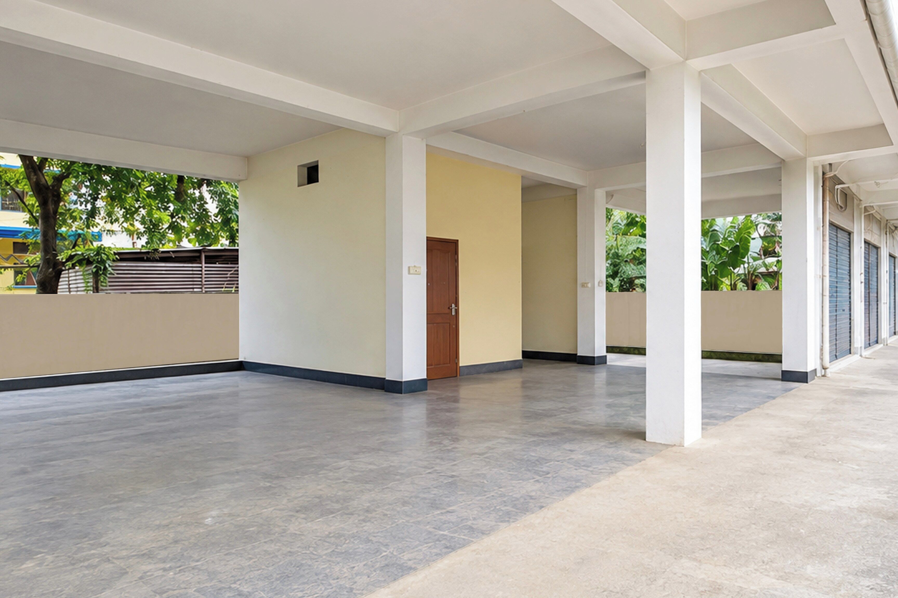 A spacious indoor area with a concrete floor, white walls, and a wooden door.