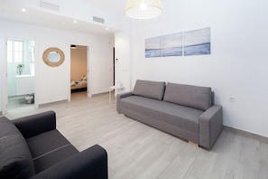 A modern living room with a grey sofa, a round mirror, and a painting of a landscape. - Spacious 5-bedroom apartment next to the Cathedral (Sevilla)