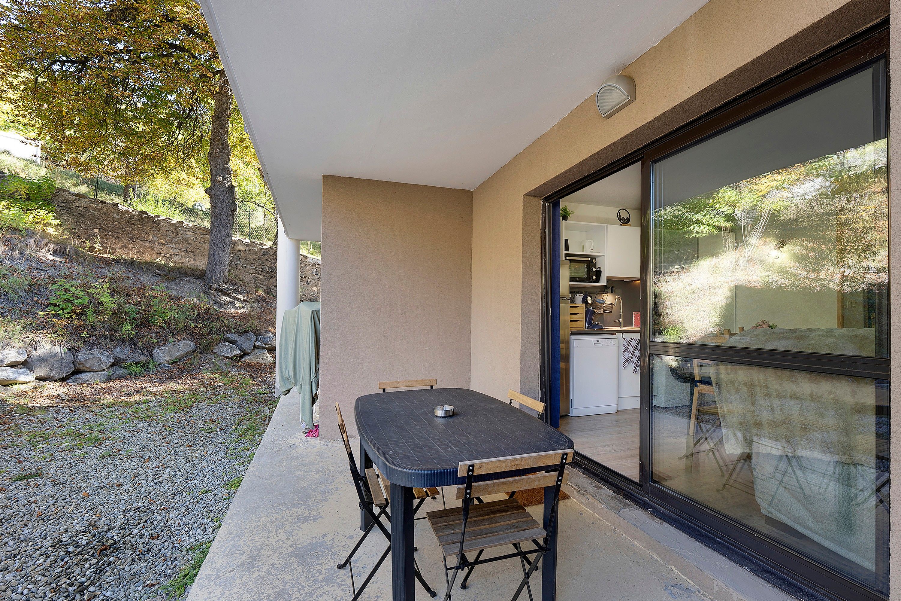 Un patio con mesa y sillas, un muro de piedra y una puerta de cristal que da a una cocina.