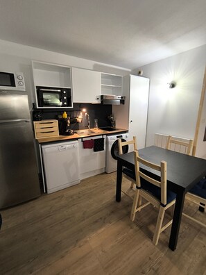 Cocina compacta equipada con microondas, horno, lavavajillas y una mesa de comedor con sillas.
