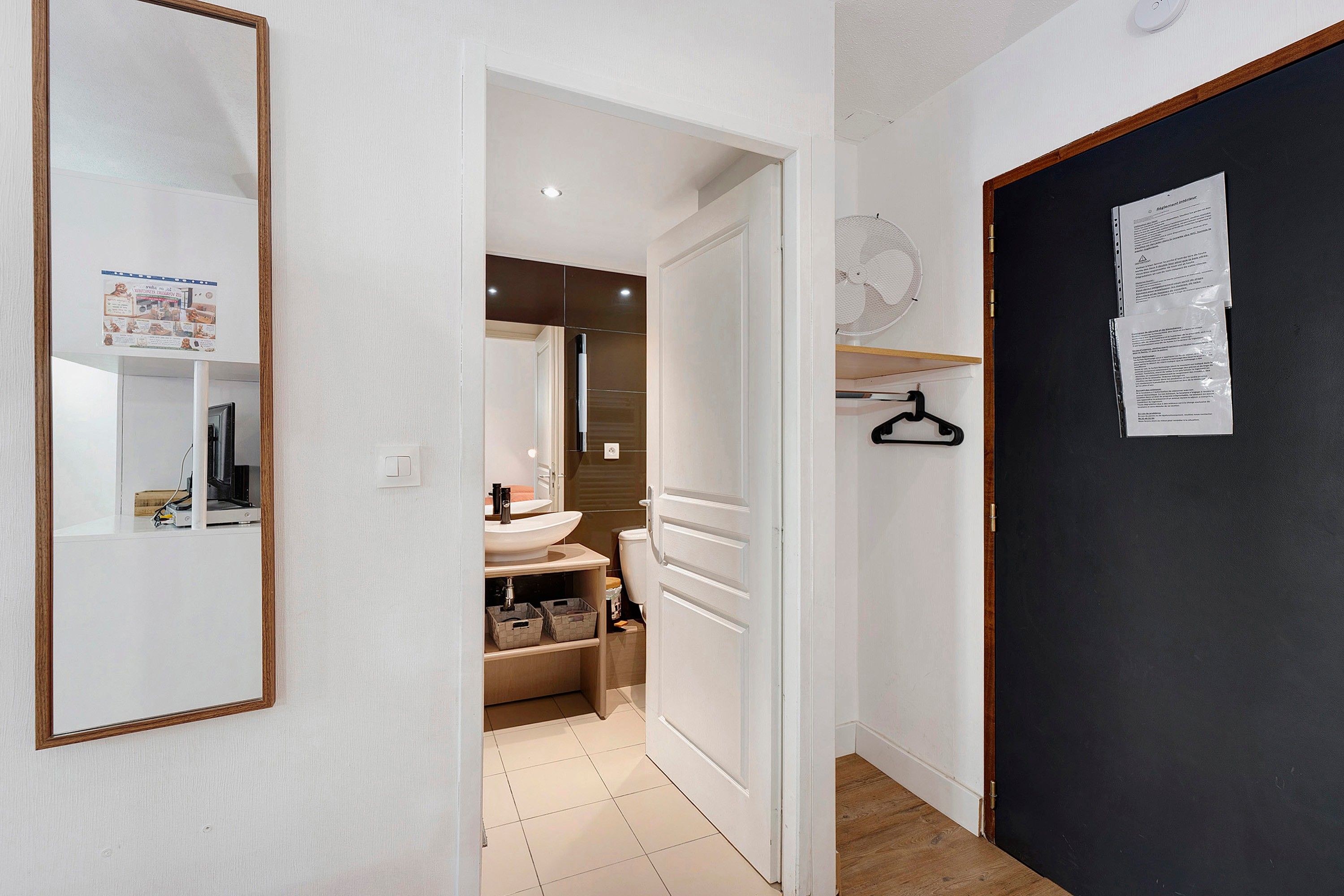 A hallway leading to a bathroom with a toilet, sink, and storage bins.
