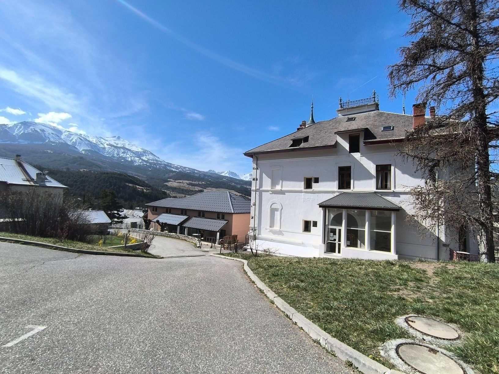 Un bâtiment à deux étages, doté d’une façade blanche, d’une entrée abritée et offrant une vue sur des montagnes enneigées en arrière-plan.