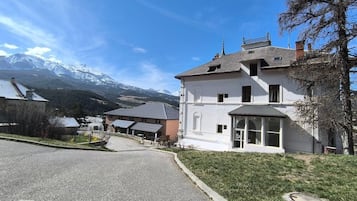 Un bâtiment à deux étages, doté d’une façade blanche, d’une entrée abritée et offrant une vue sur des montagnes enneigées en arrière-plan.
