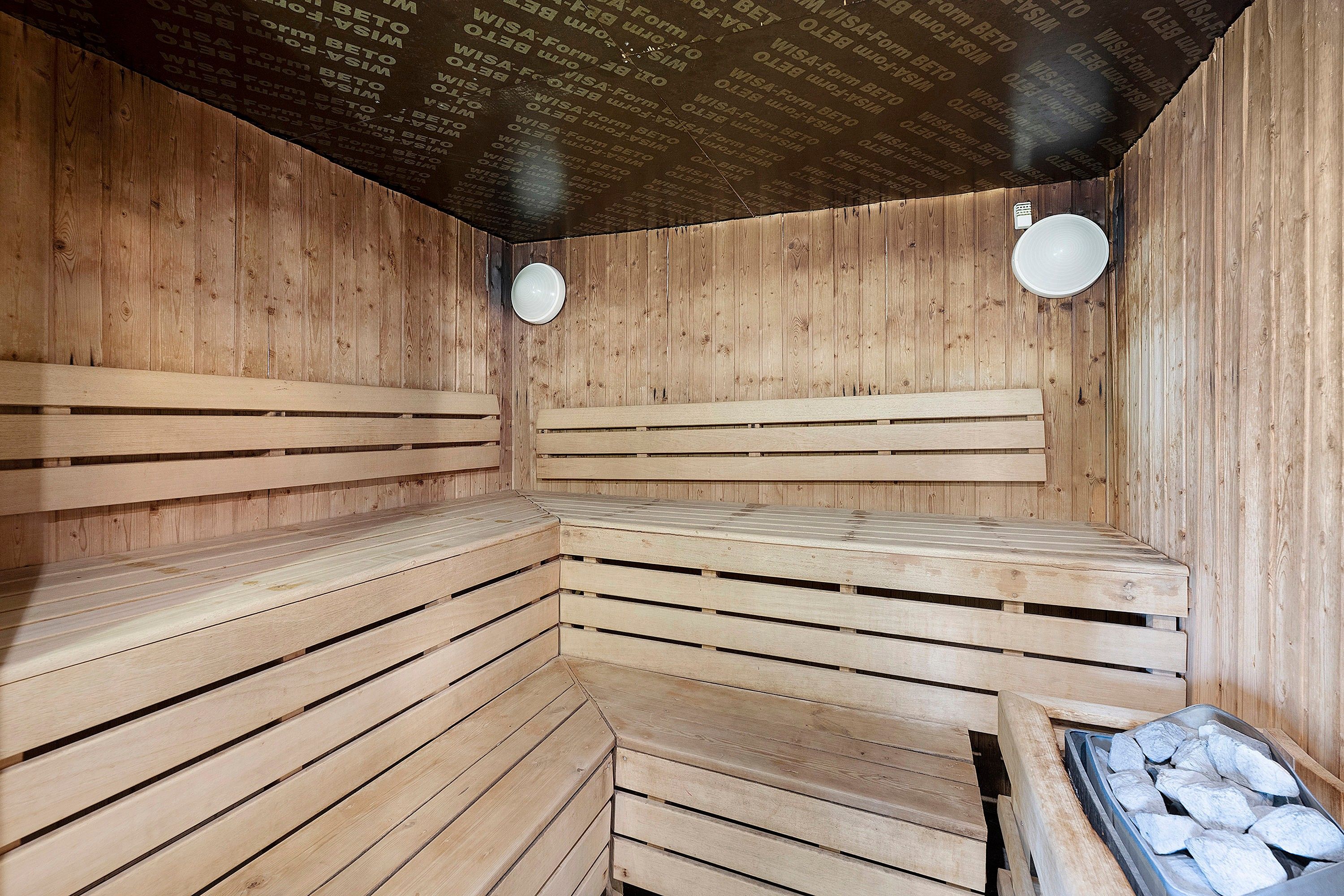 Un sauna avec des bancs en bois et un mur orné d’un motif répétitif.
