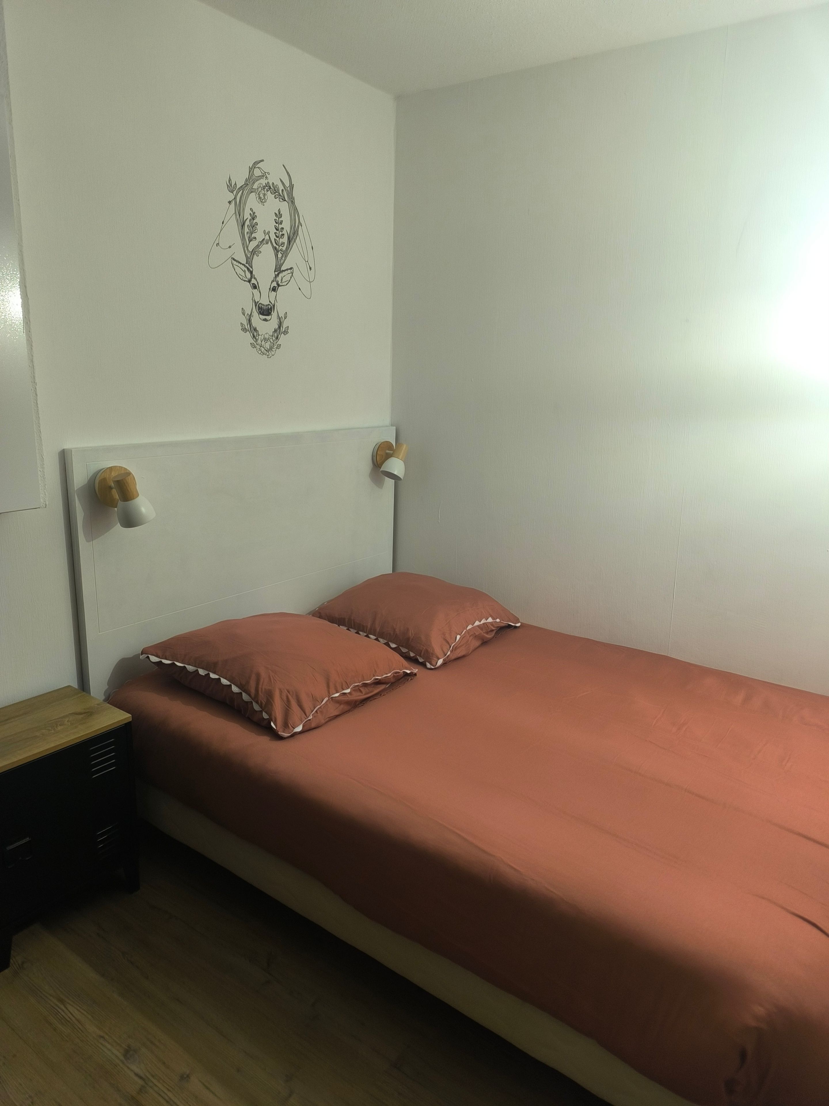 Un lit simple avec une tête de lit, une table de chevet et un luminaire fixé au mur.