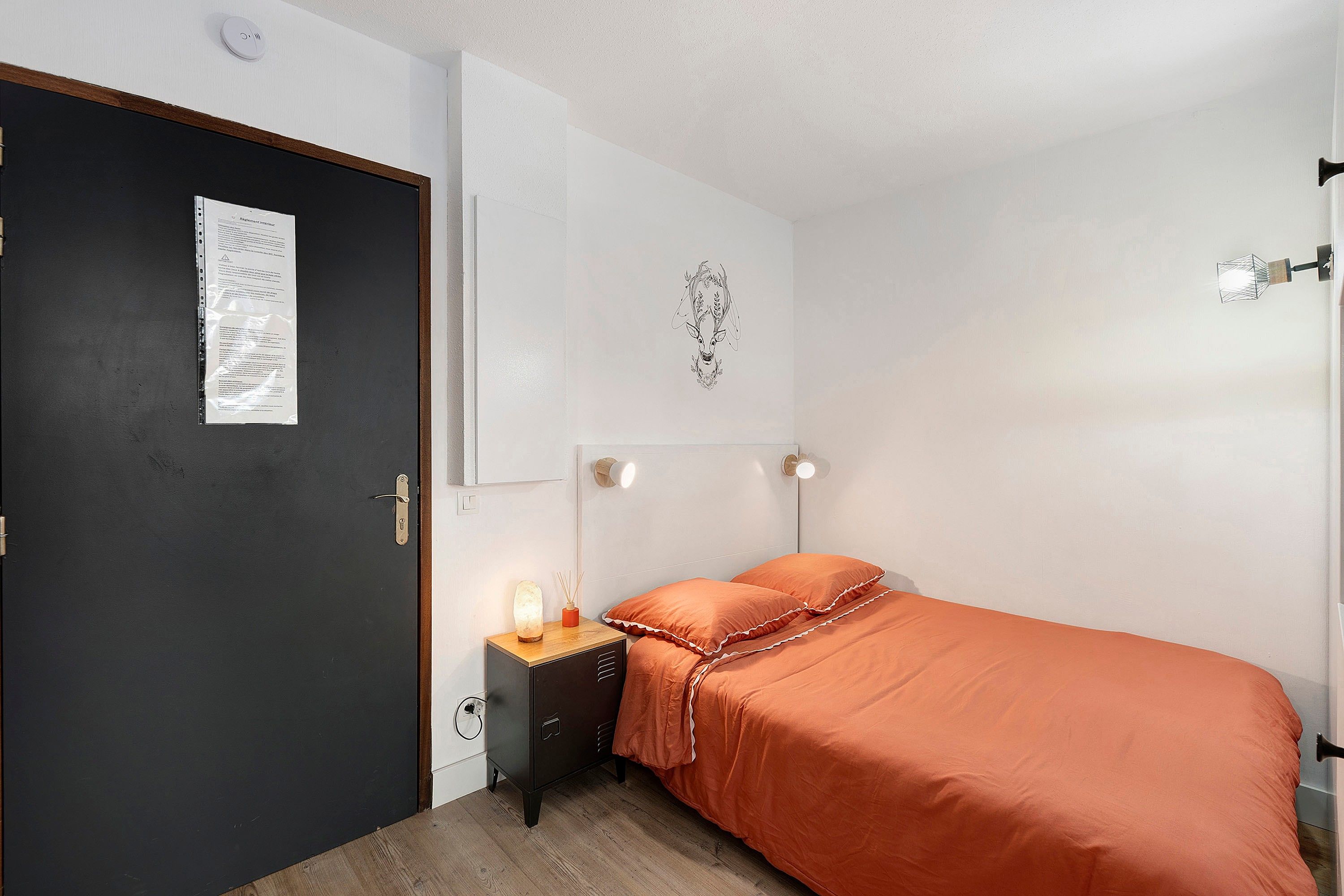 Ein Schlafzimmer mit Bett, Nachttisch, Wandlampe und einer Tür mit einem Hinweis.