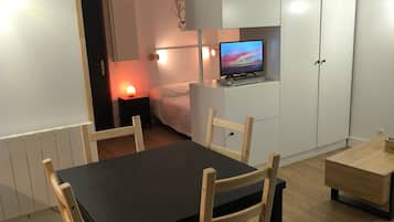 A room with a dining table, chairs, a bed, a TV, and a wardrobe.