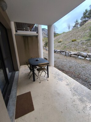 Un patio exterior con una mesa y sillas, un felpudo y vistas a una ladera rocosa.
