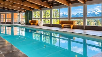 Une piscine dotée de bancs en bois et de grandes fenêtres offrant une vue sur les montagnes.