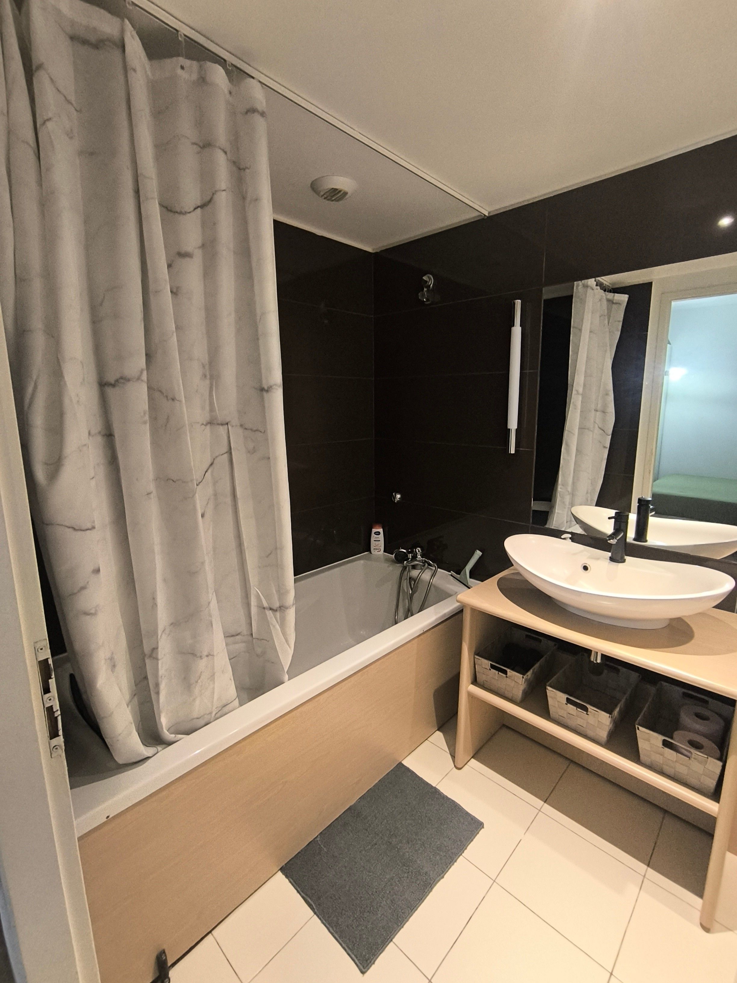 A modern bathroom with a bathtub, two sinks, a shower, and a large mirror.