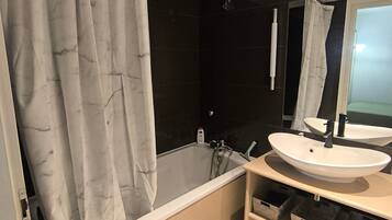A modern bathroom with a bathtub, two sinks, a shower, and a large mirror.