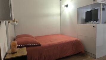 A bedroom with a bed, a nightstand, a heater, a television on a cabinet, and a wall-mounted light.