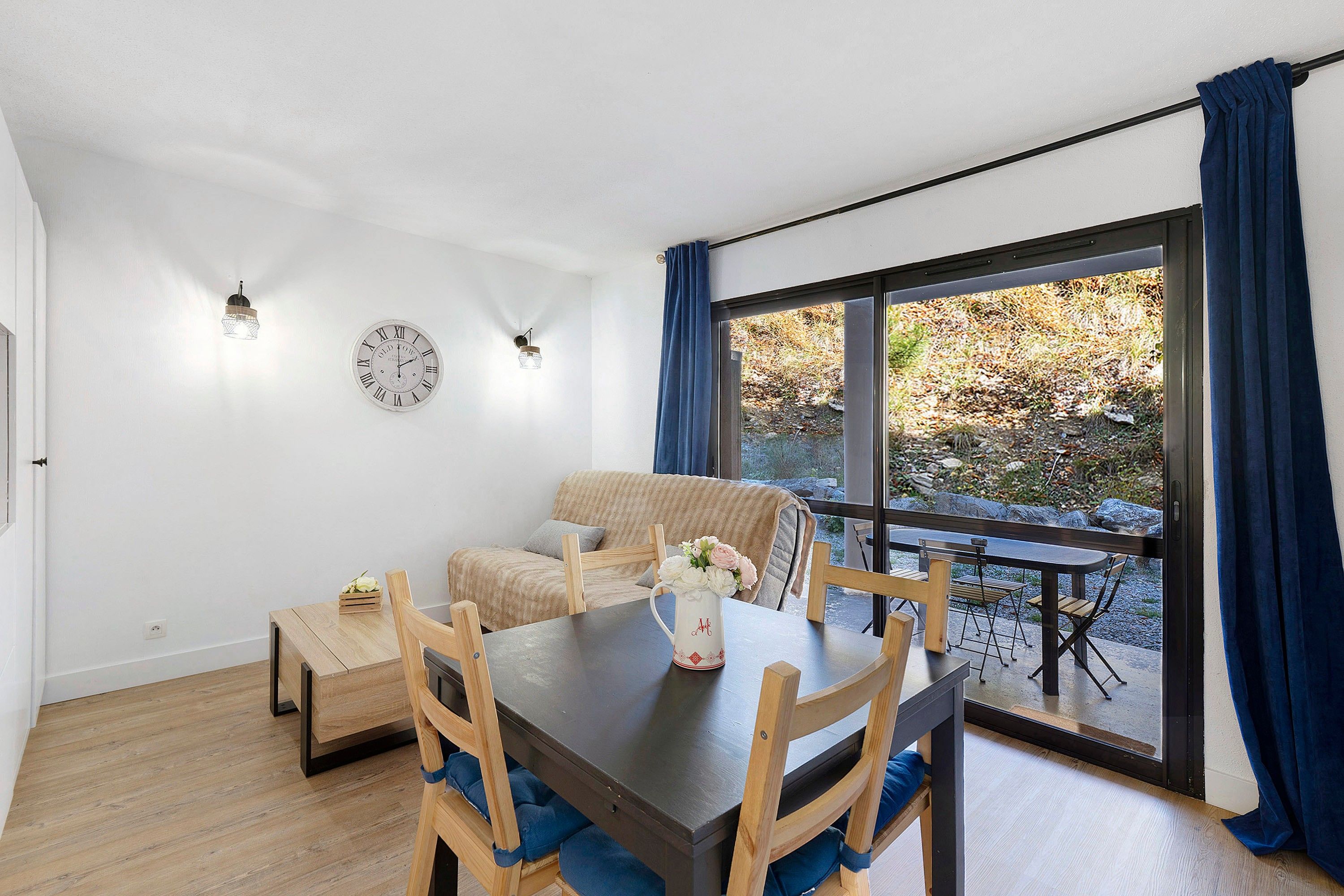 Ein modernes Wohnzimmer mit Esstisch, Stühlen, einer Couch und einem großen Fenster mit Vorhängen.
