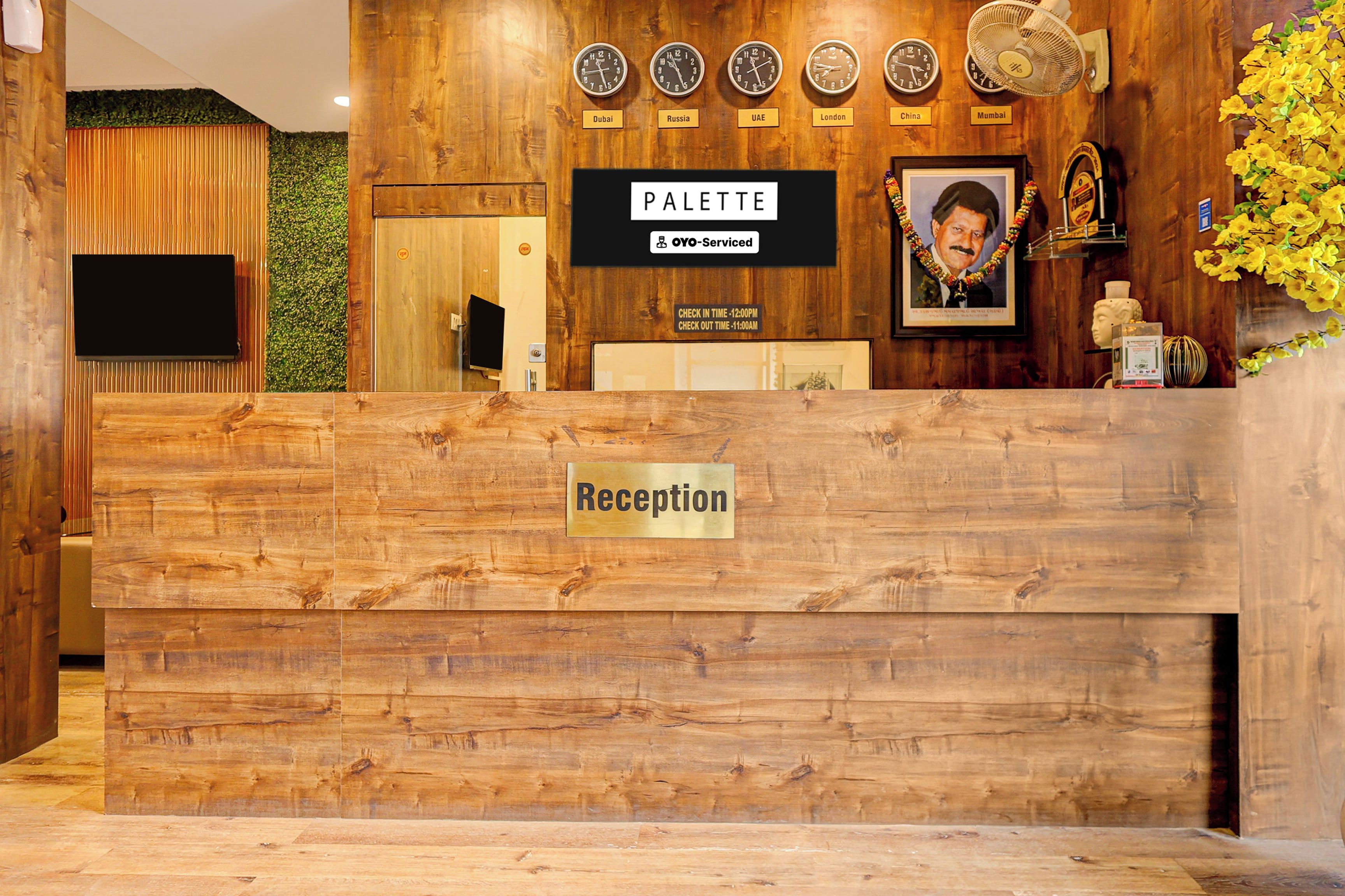 En receptionsdisk med träpanel, en skylt som visar ”Reception”, och en skylt med texten ”PALETTE” ovanför klockor som är märkta med olika stadsnamn.