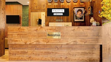En receptionsdisk med träpanel, en skylt som visar ”Reception”, och en skylt med texten ”PALETTE” ovanför klockor som är märkta med olika stadsnamn.